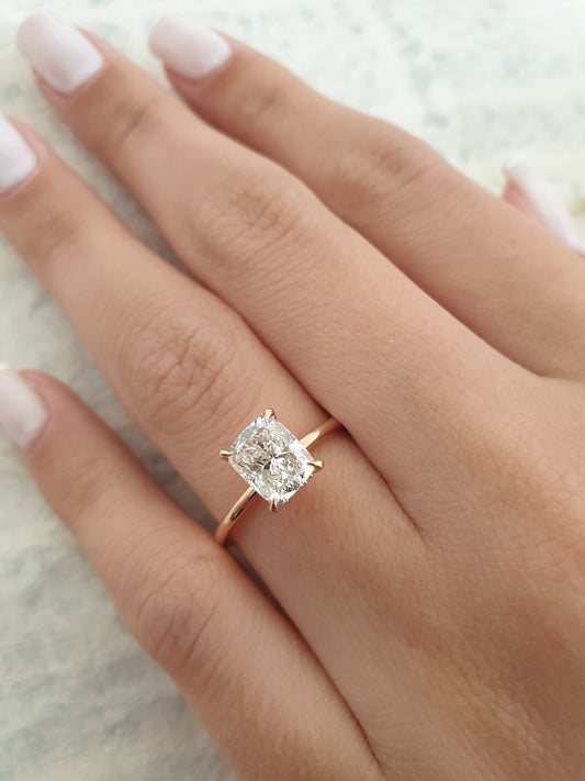 Close-up of a cushion-cut diamond engagement ring set in rose gold on a woman's hand, showcasing brilliance and elegance.